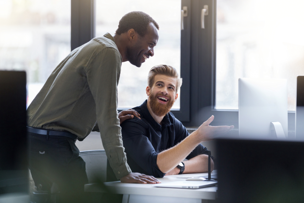 Two smiling men in an office with computers